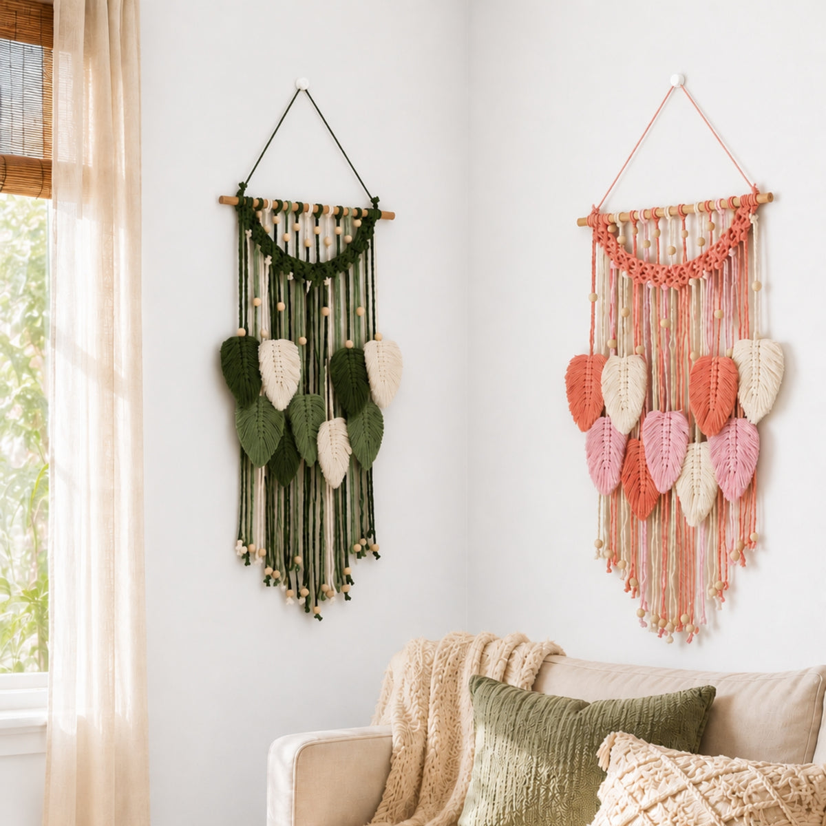 Two boho-style woven wall hangings with leaf motifs are displayed on a white wall above a sofa in a living room. The left hanging is green, and the right hanging is in coral pink and peach tones.